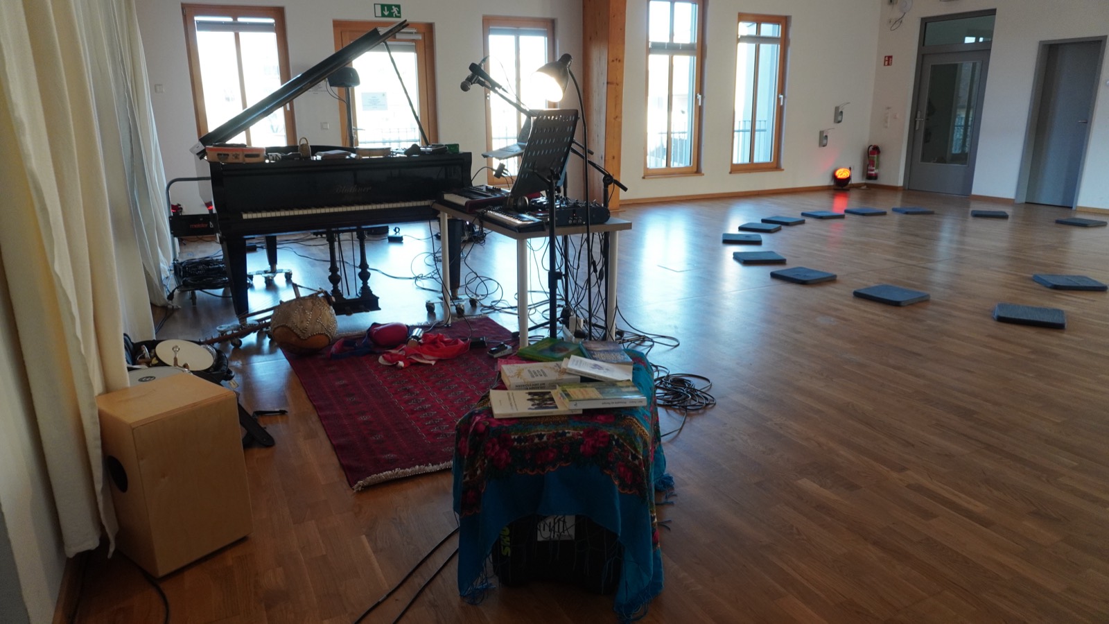 Flügel, Instrumenten-Setup und Teppich im Workshopraum, daneben eine Reihe Sitzkissen