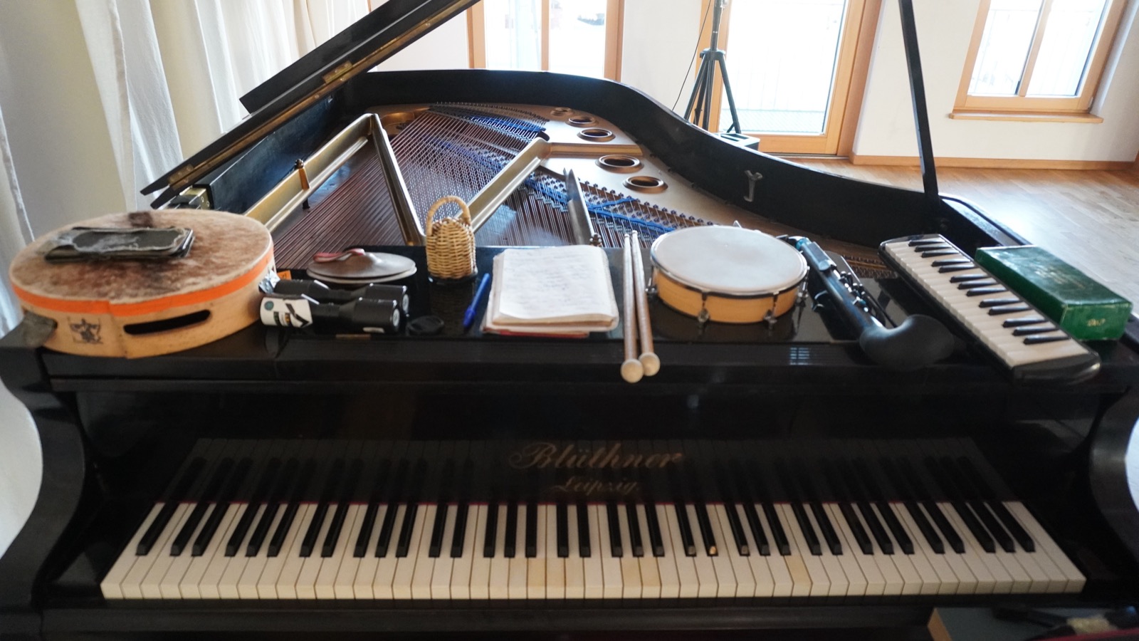 An open grand piano prepared with frame drums, mallets, melodica and kalimba